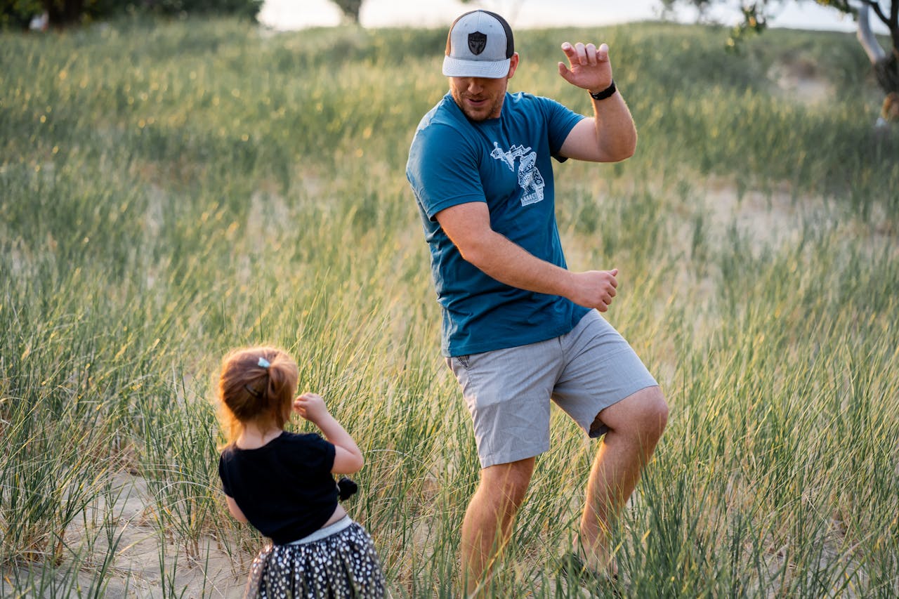 services-01 A father dances playfully with his daughter in a sunny field, capturing joy and bonding.