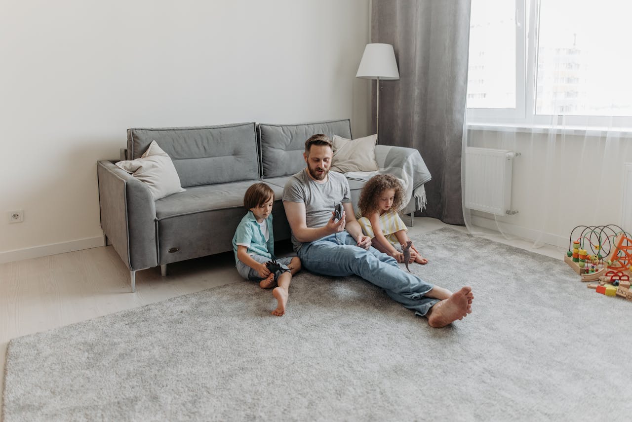 services-02 Father and two children enjoy playtime in the living room. Warm family bonding moment captured indoors.